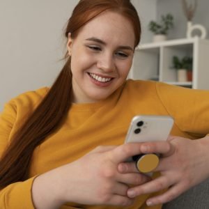 portrait woman using her smartphone home couch by holding from pop socket